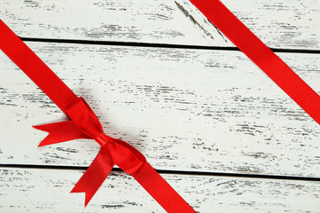 Red ribbon with bow on white wooden background