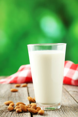 Glass of milk with almonds on white wooden background