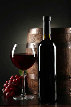 Red wine glass with bottle and barrel on black background