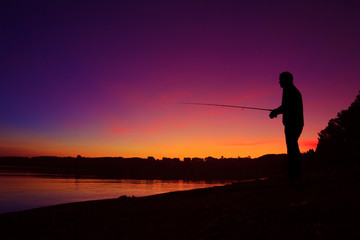 Silhouette of a man fishing on the lake shore at sunset
