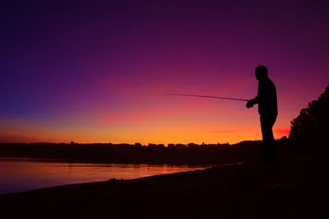 Fotobehang Silhouette of a man fishing on the lake shore at sunset © nevodka.com