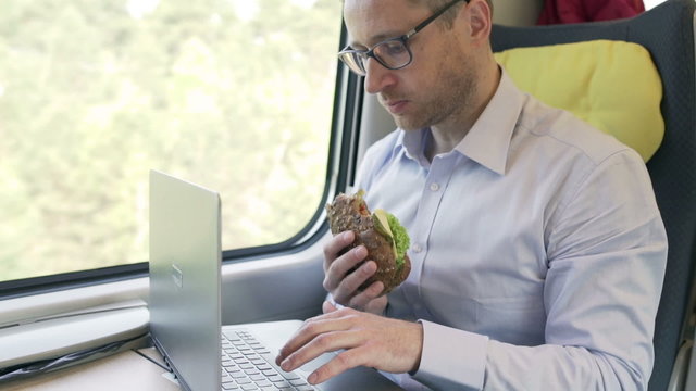 Businessman eating sandwich and working on laptop, steadycam shot
