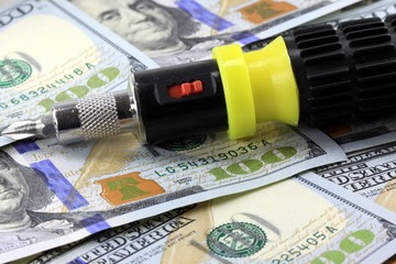 Financial Tools screwdriver laying on one hundred dollar bills