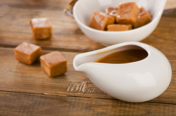 Caramel candies and sauce on  rustic wooden table.