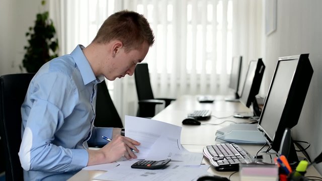 man working in the office - writing on paper with pen and counting on a calculator - documents