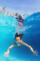 Young happy smiling child swimming underwater in the blue pool