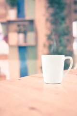 Vintage filter : White coffee cup on wood table at blur cafe bac