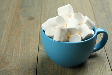 Fototapeta na wymiar Marshmallow in a blue cup on a wooden background
