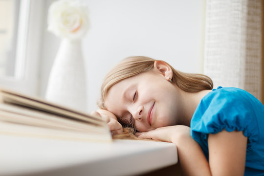 Little girl sleeping on windowsill with book