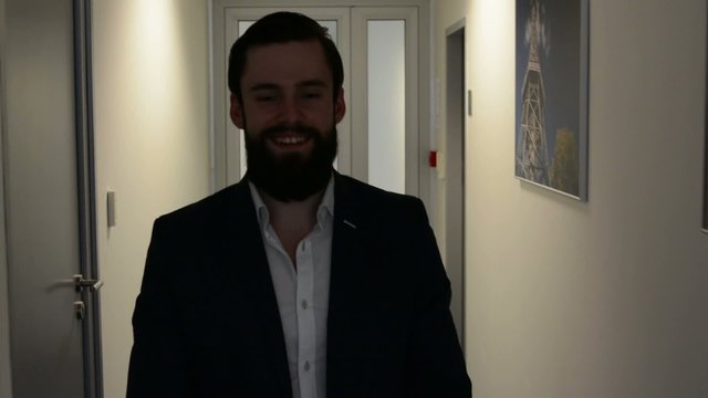 young handsome man with full-beard (hipster) walks and smiles to camera in the office - steadicam