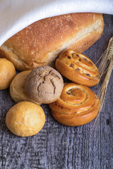Different types of fresh bread and wheat ears on old wooden tabl