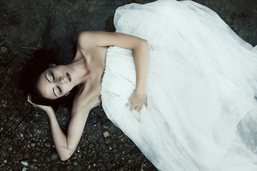 Naklejka premium Woman lying on the shore in white dress, dark mystery scene 