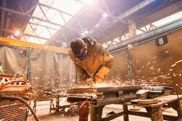 Young man in protective workwear welding in a factory - obrazy, fototapety, plakaty