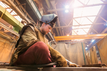 Young man in protective workwear welding in a factory
