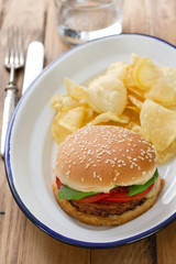 hamburger with potato chips on white dish with glass of water