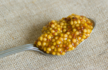Metal spoon with french mustard on a gray sackcloth