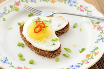 Fried egg heart rye sandwich with scallion, chili and fork on wh