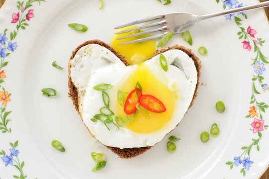 Fried egg heart rye sandwich with scallion, chili and fork on wh