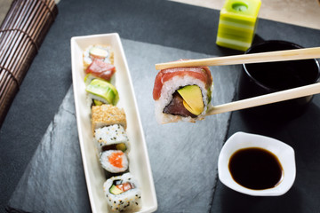 Hand holding sushi roll using chopsticks / taking portion sushi