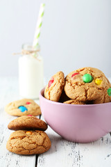Cookies with colorful candy in bowl on white wooden background