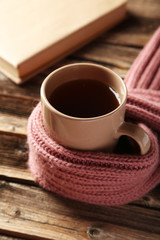 Cup of coffee with warm scarf on brown wooden background
