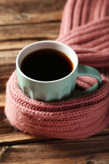 Cup of coffee with warm scarf on brown wooden background