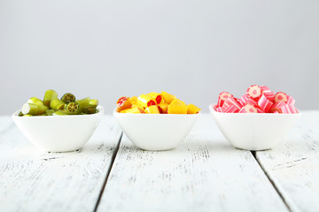 Colorful candies in bowl on white wooden background