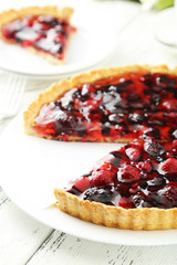 Fresh berry tart on plate on white wooden background