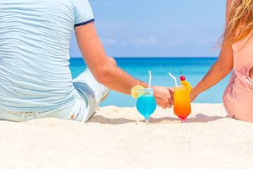young happy couple enjoying tropical cocktails on sand beach