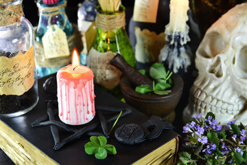 Bloody candle on witch book with magic objects and clover