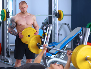 Obraz premium Young man lifting the barbell in gym with instructor