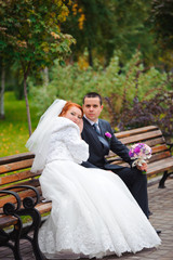 Bride and groom on bench in autumn park