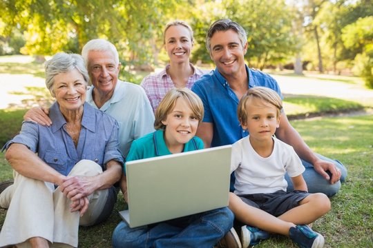 Happy family smiling at camera and using laptop in the park