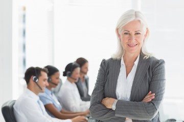 Obraz premium Businesswoman with arms crossed and executives using computers