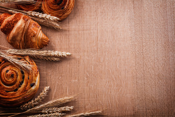 Composition of wheat ears bakery products on oaken wooden board  - obrazy, fototapety, plakaty