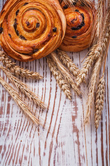 Fresh-baked raisin buns wheat ears on vintage wooden board food 
