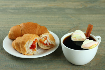 A cup of hot chocolate with marshmallows and croissants on the wooden background