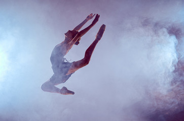 Beautiful young ballet dancer jumping on a lilac background. 