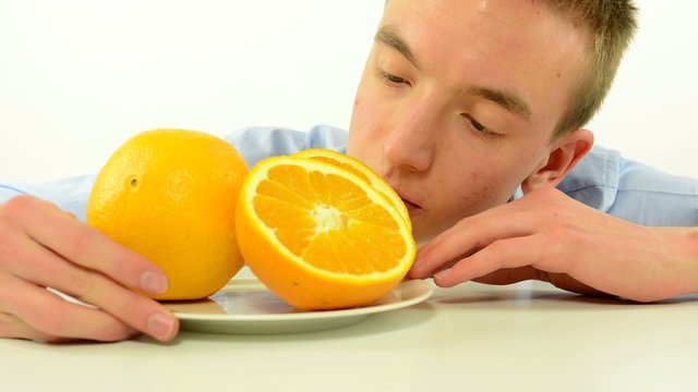 man looks on orange and smiles to camera - fruits - white background studio