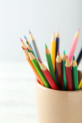 Colorful pencils in cup on white wooden background