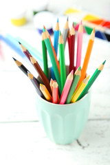 Colorful pencils in cup on white wooden background
