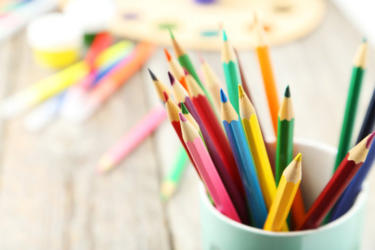 Colorful pencils in cup on grey wooden background
