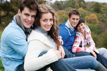 Fototapeta premium Two couples sit together outside and smile for the camera.