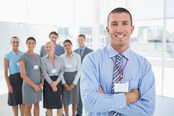Obraz premium Businessman smiling at camera with team behind him