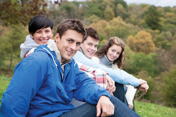 Fototapeta premium Four friends sit together outdoors and smile for the camera