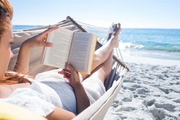 Brunette reading a book while relaxing in the hammock - obrazy, fototapety, plakaty