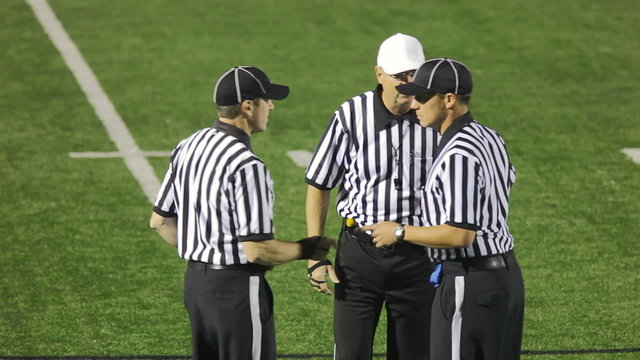 Three football referees discuss a  pass interference as the penalty call