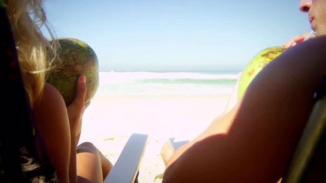 Brazilian couple sit on a beach drinking fresh Coconut water