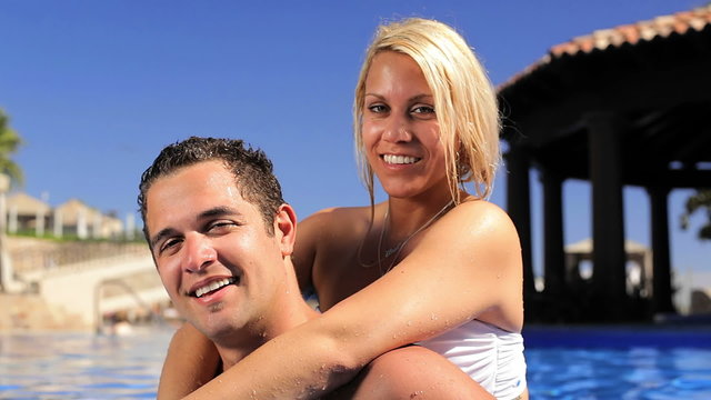 A cute couple kiss and hug in a beautiful pool while on vacation