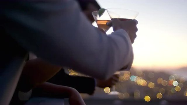 Friends hang out and drink cocktails on a rooftop bar at sunset in San Francisco
